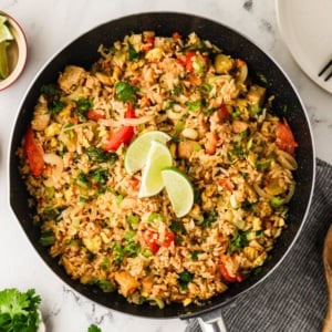 Skillet filled with vegetarian Thai fried rice topped with lime wedges and fresh herbs.