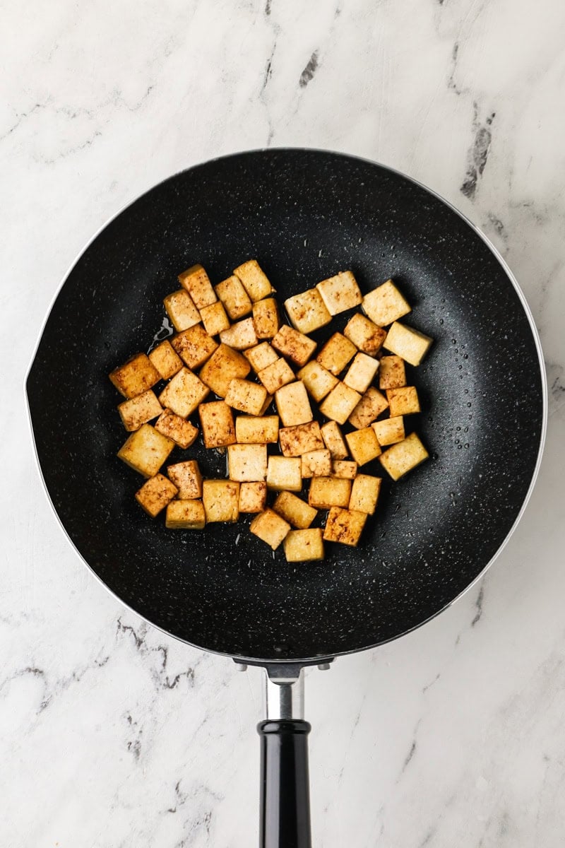 Golden-brown tofu cubes cooking in a skillet for vegetarian Thai fried rice.