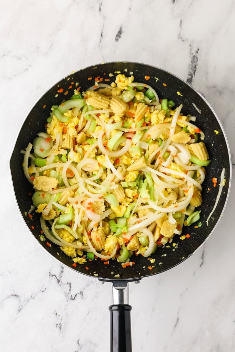 Onions, bok choy stems, carrots, and baby corn stir-frying in a skillet.
