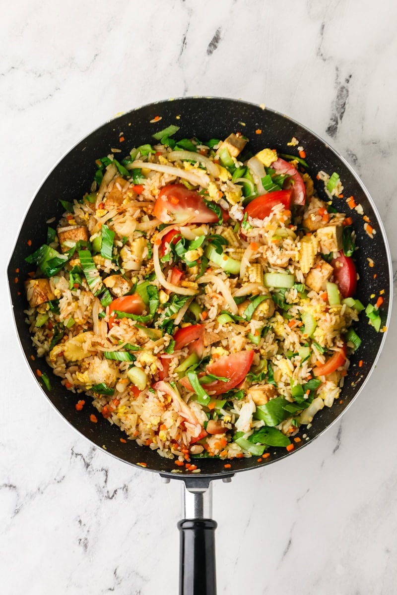 Thai fried rice cooking with tomatoes and bok choy leaves added to the pan.