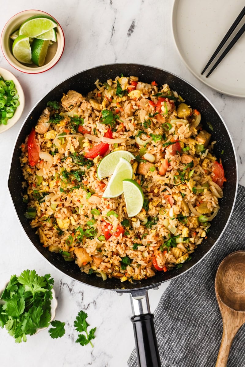 Finished vegetarian Thai fried rice garnished with cilantro, spring onions, and lime wedges.
