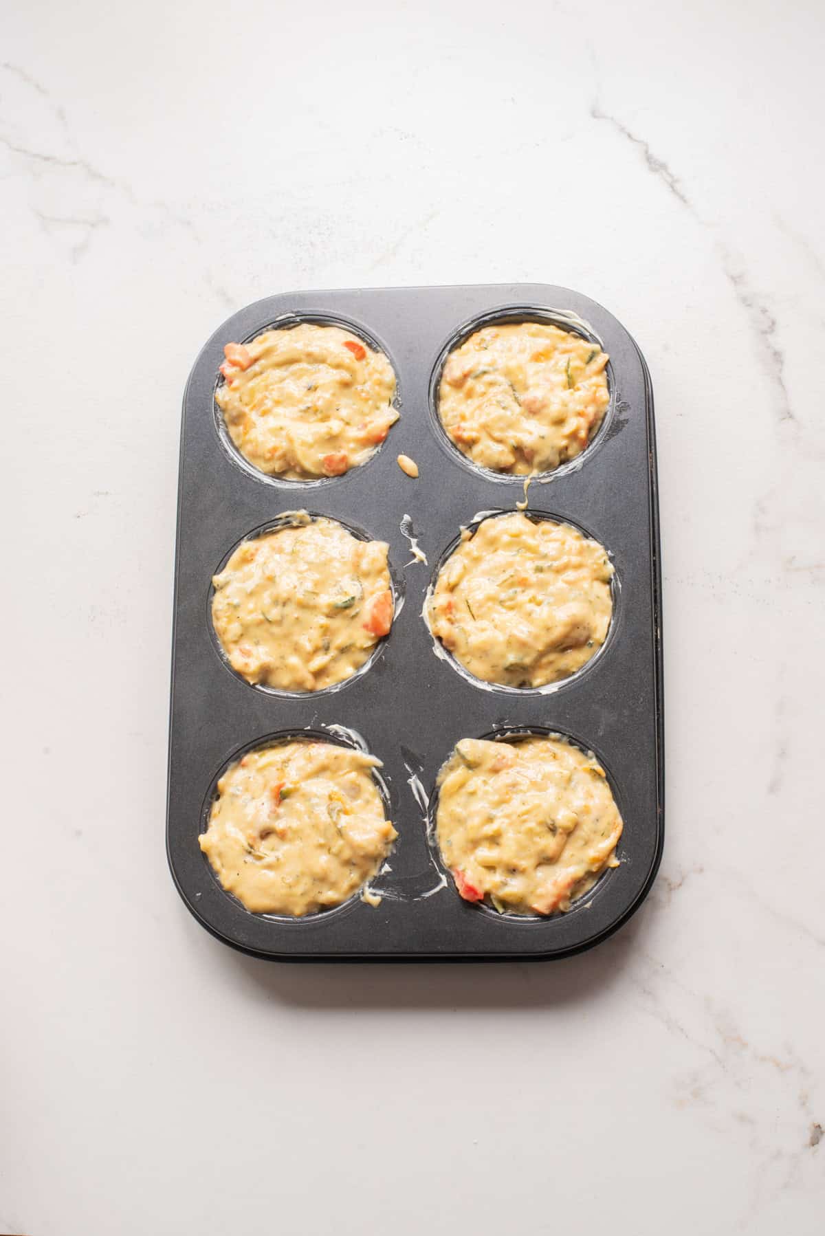 An overhead image of adding the veggie muffin batter to the muffin tin.