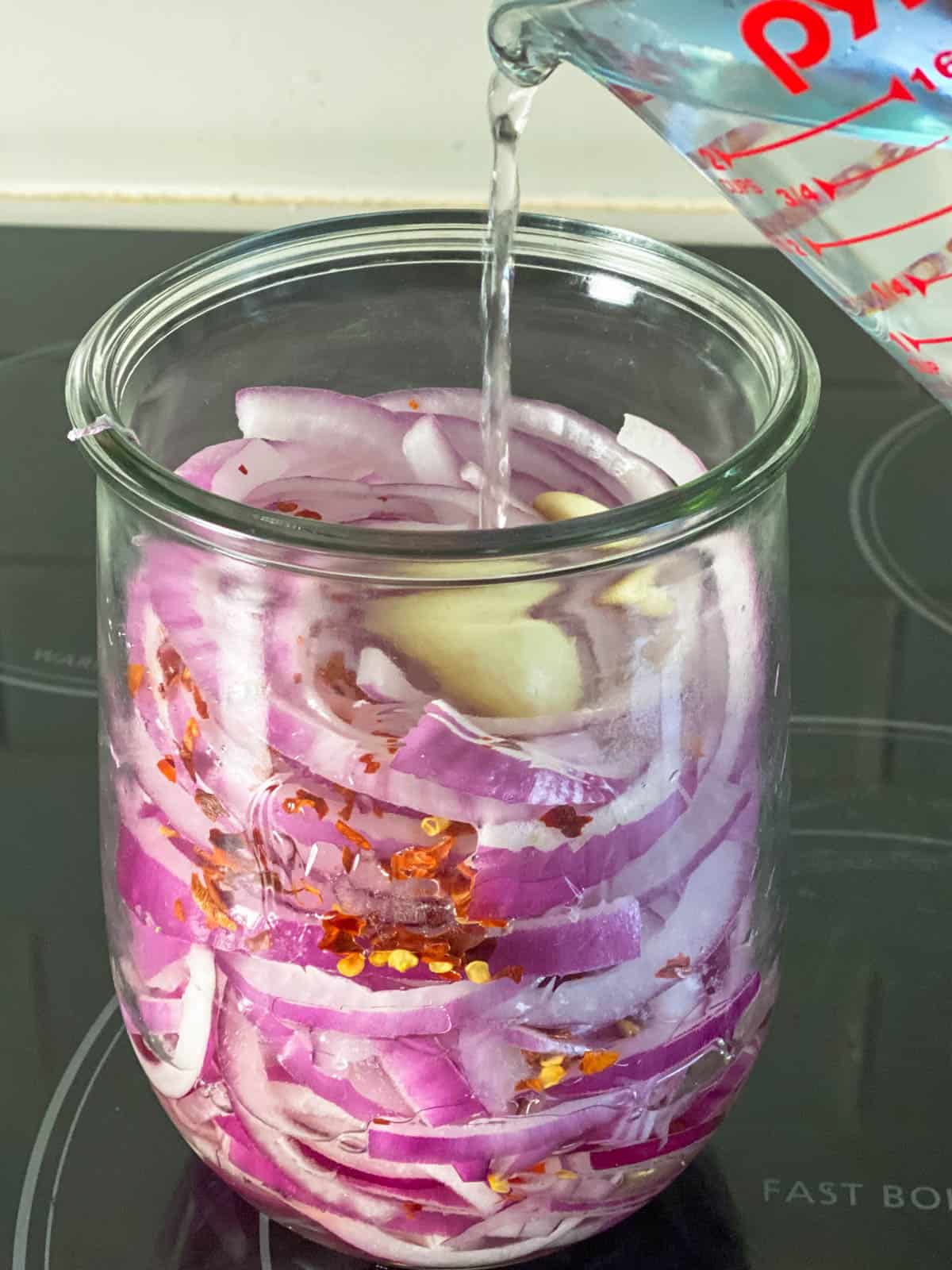 Pouring pickling liquid into jar with onions