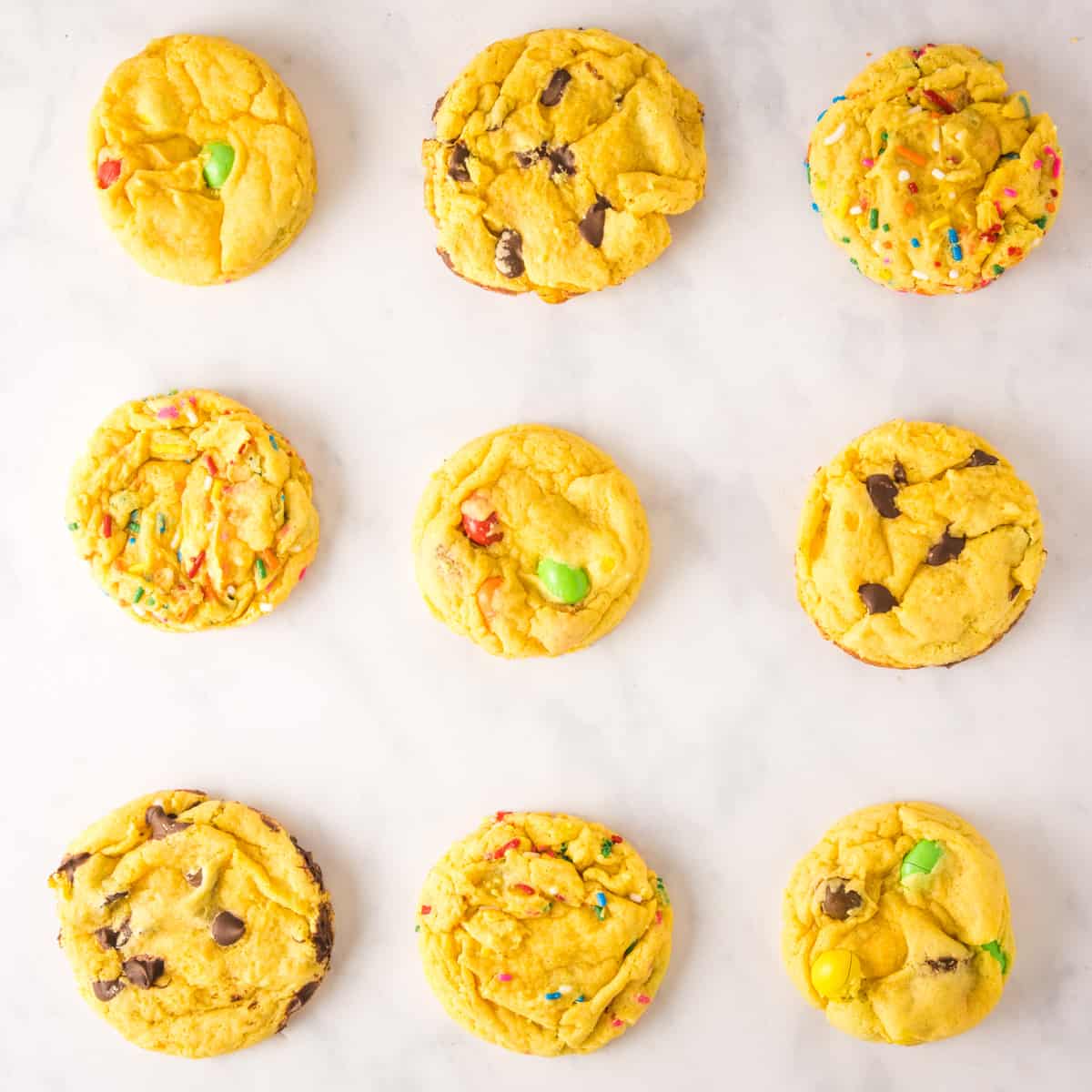 Overhead view of 9 yellow cake mix cookies on a white marble background.