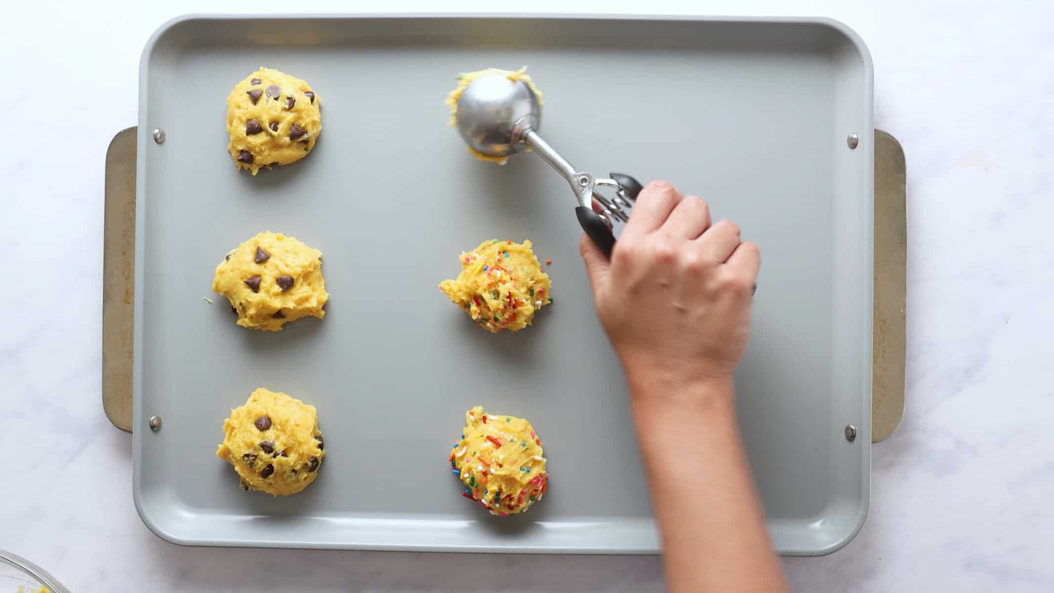 Hand using cookie scoop to place cookie dough balls on the baking sheet.