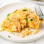 A serving of yellow squash casserole with a golden cracker topping on a white plate.