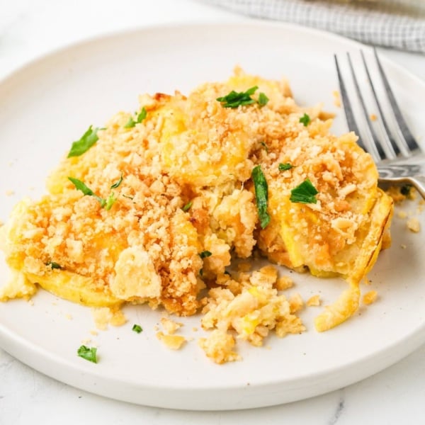 A serving of yellow squash casserole with a golden cracker topping on a white plate.