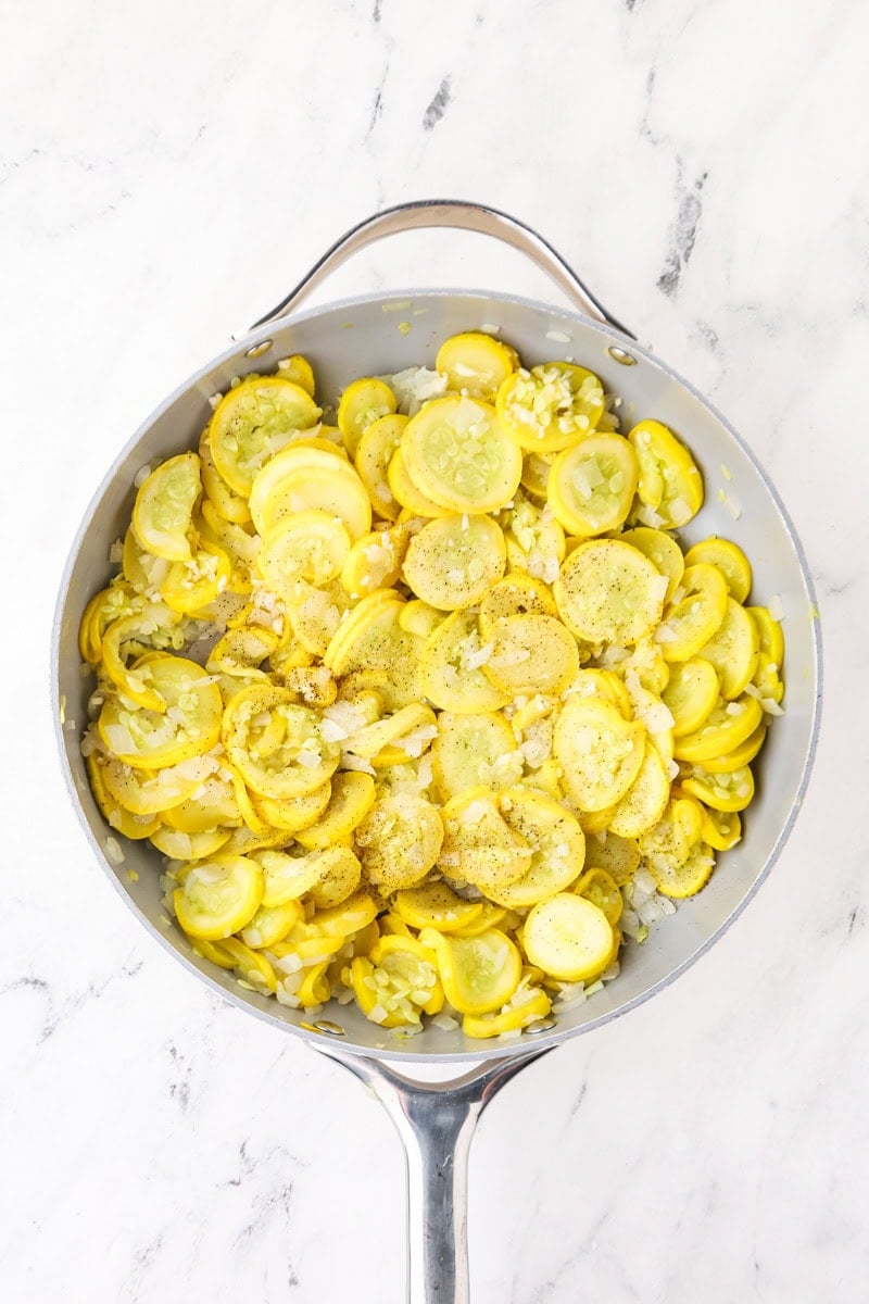 Cooked yellow squash and onion seasoned with garlic, salt, and black pepper in a skillet.