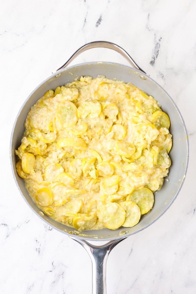 Creamy yellow squash mixture combined with eggs, sour cream, cheddar, and Parmesan in a skillet.