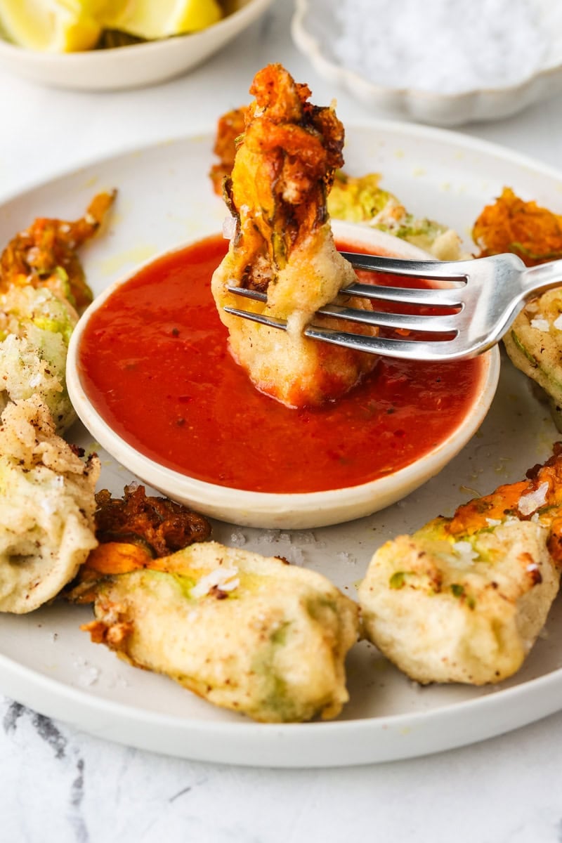 Crispy ricotta-stuffed zucchini blossom dipped into marinara sauce with a fork.