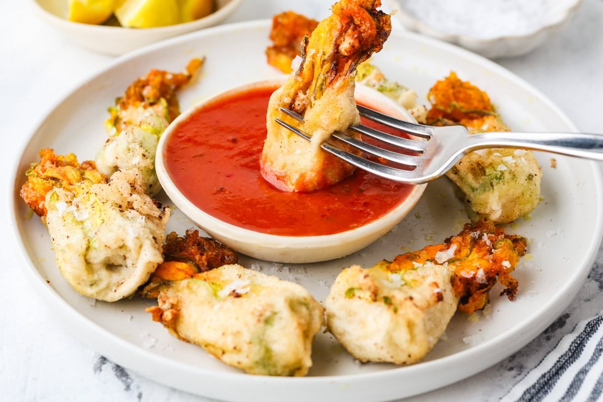 Crispy ricotta-stuffed zucchini blossom dipped into marinara sauce with a fork.