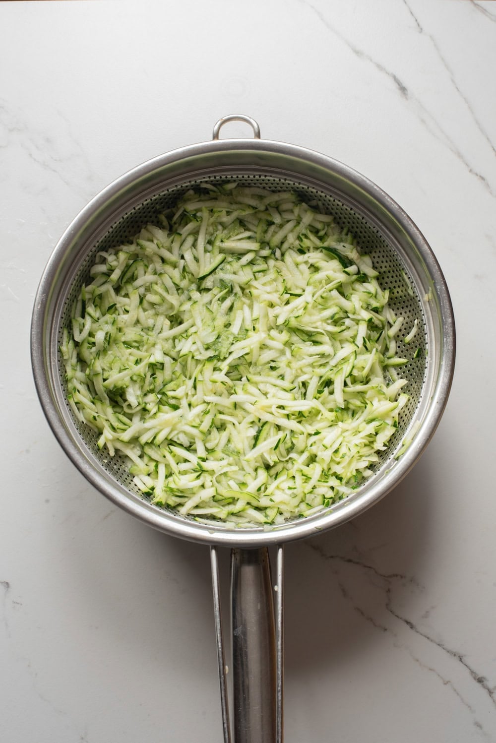 Shredded zucchini draining in a colander before making zucchini fritters.