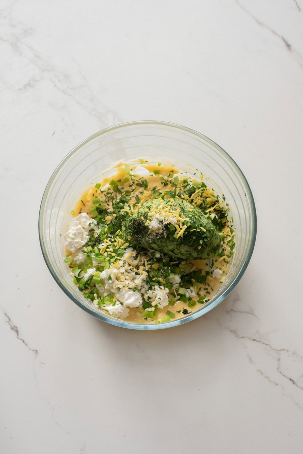 Zucchini fritter batter with feta, herbs, and green onions mixed in a bowl.