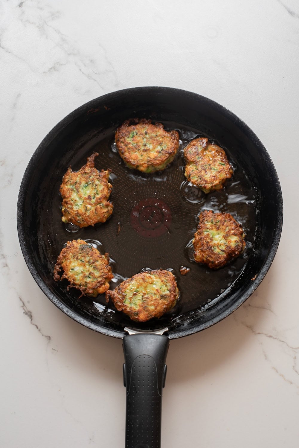Zucchini fritters cooking in a skillet until golden brown.