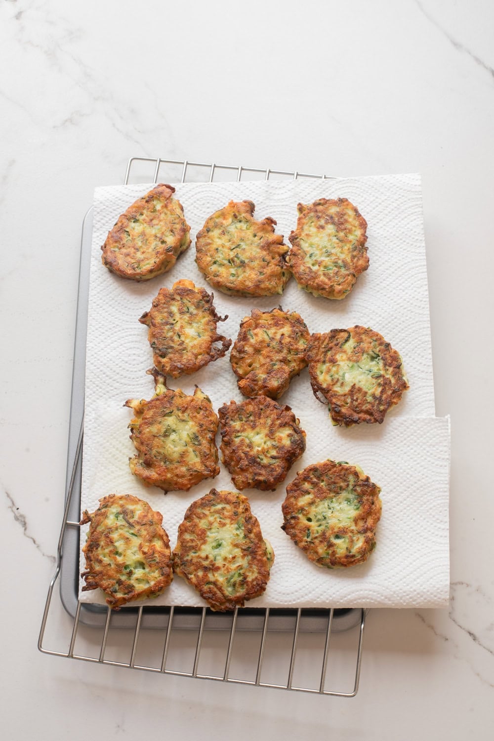 Cooked zucchini fritters cooling on a wire rack lined with paper towels.