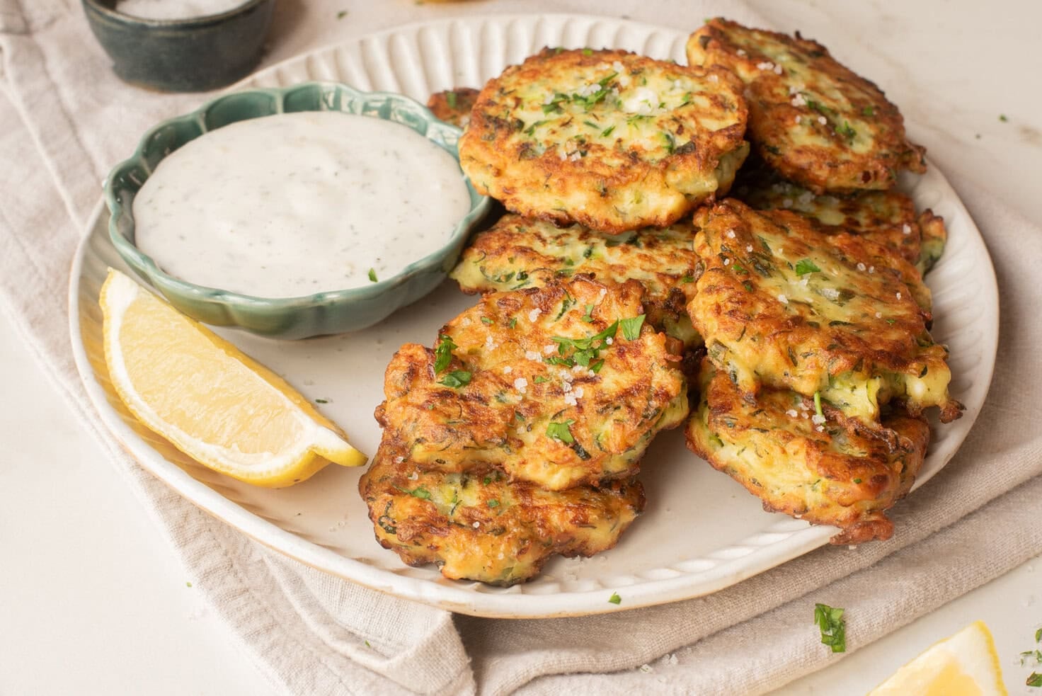 Plate of crispy zucchini fritters served with lemon wedges and lemon dill yogurt sauce.