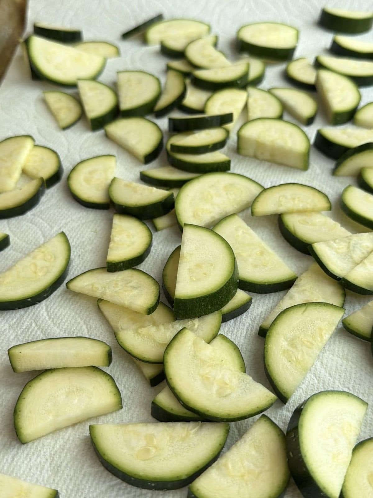Salted zucchini half moons resting on paper towels after slicing.