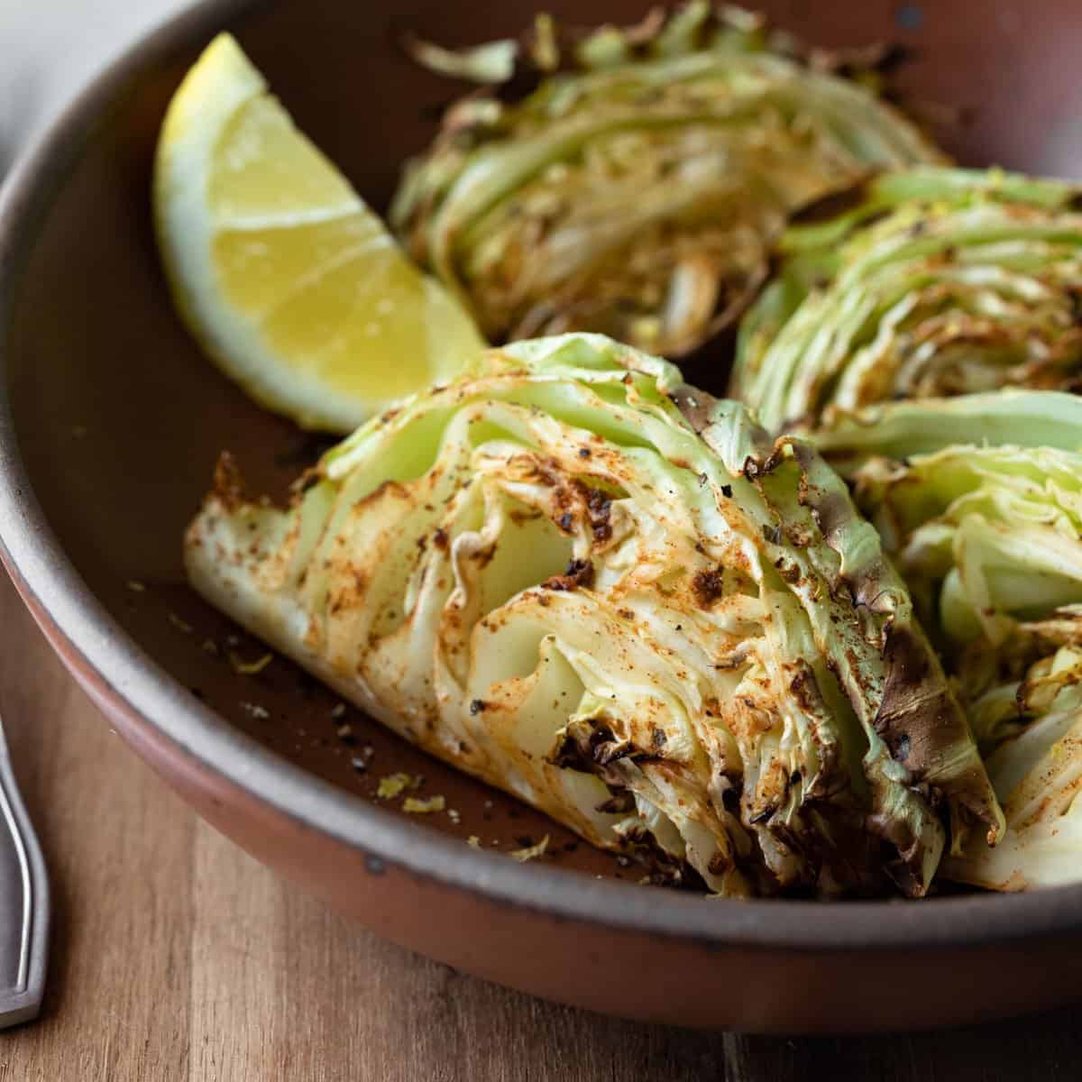 A close-up shot of air-fried cabbage wedges in a red bowl.