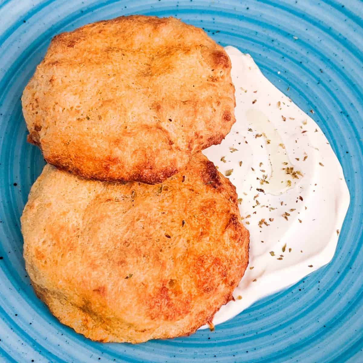 Overhead view of air fryer hash brown patties from scratch with sour cream placed on a plate.