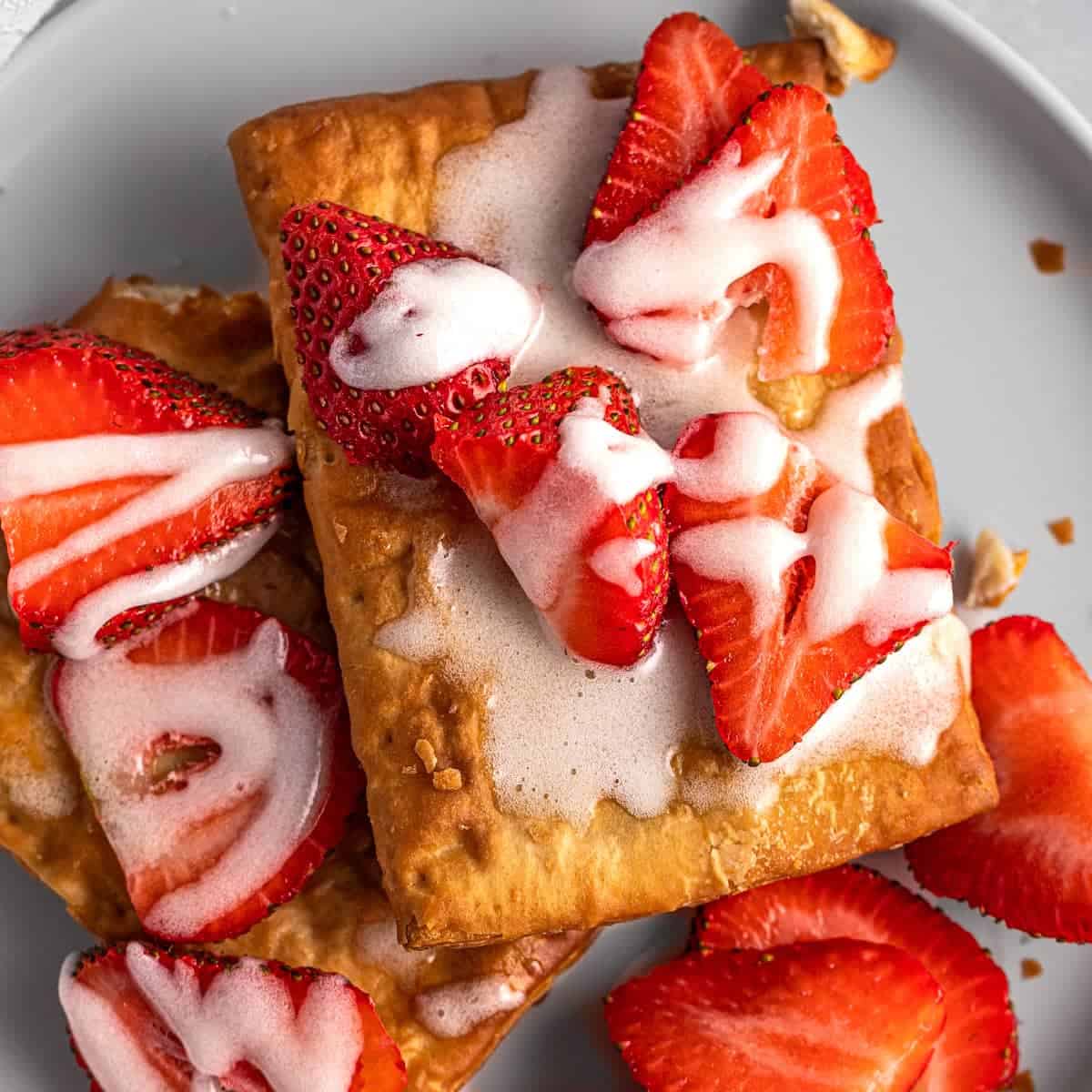 Overhead view of a crispy air-fried toaster strudel placed on a white plate with fresh strawberries on top.