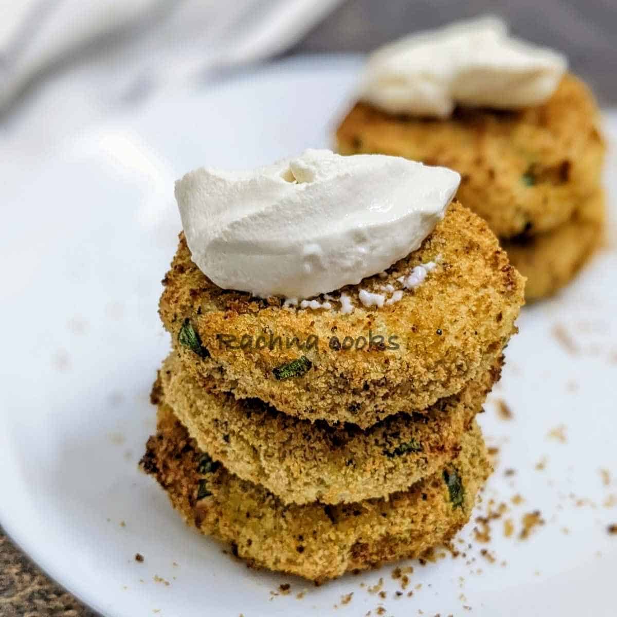 Stacked air fryer potato pancakes with sour cream dollop on top, placed on white plate.