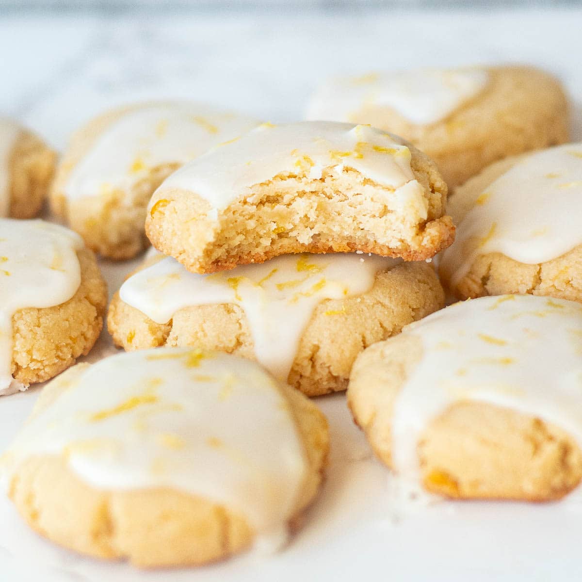 A close-up view of almond lemon cookies, one with a bite taken out on top.