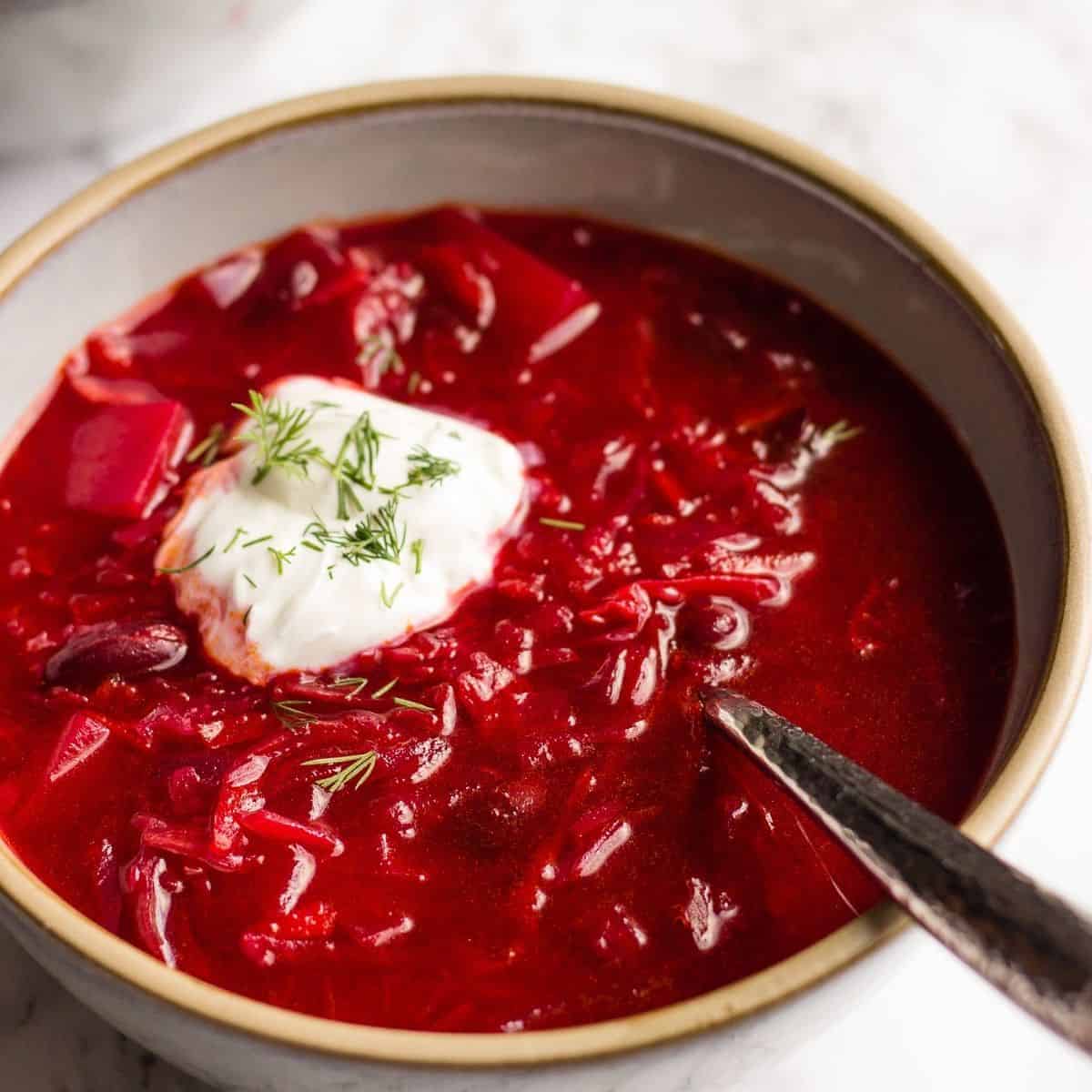 An overhead view of authentic vegan borscht placed in a grey bowl with sour cream and dill on top.