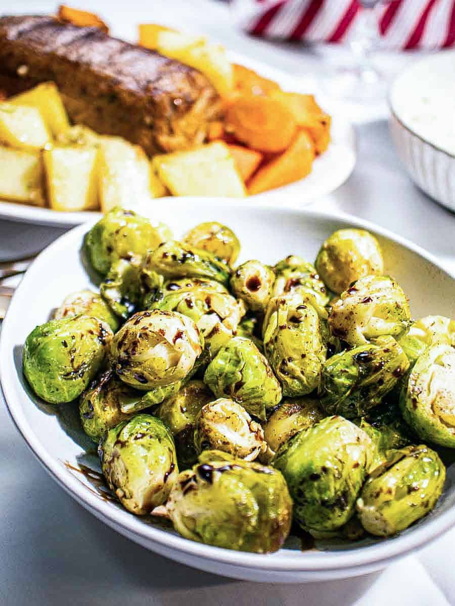 A straight view of balsamic-glazed brussels sprouts placed on a white bowl.