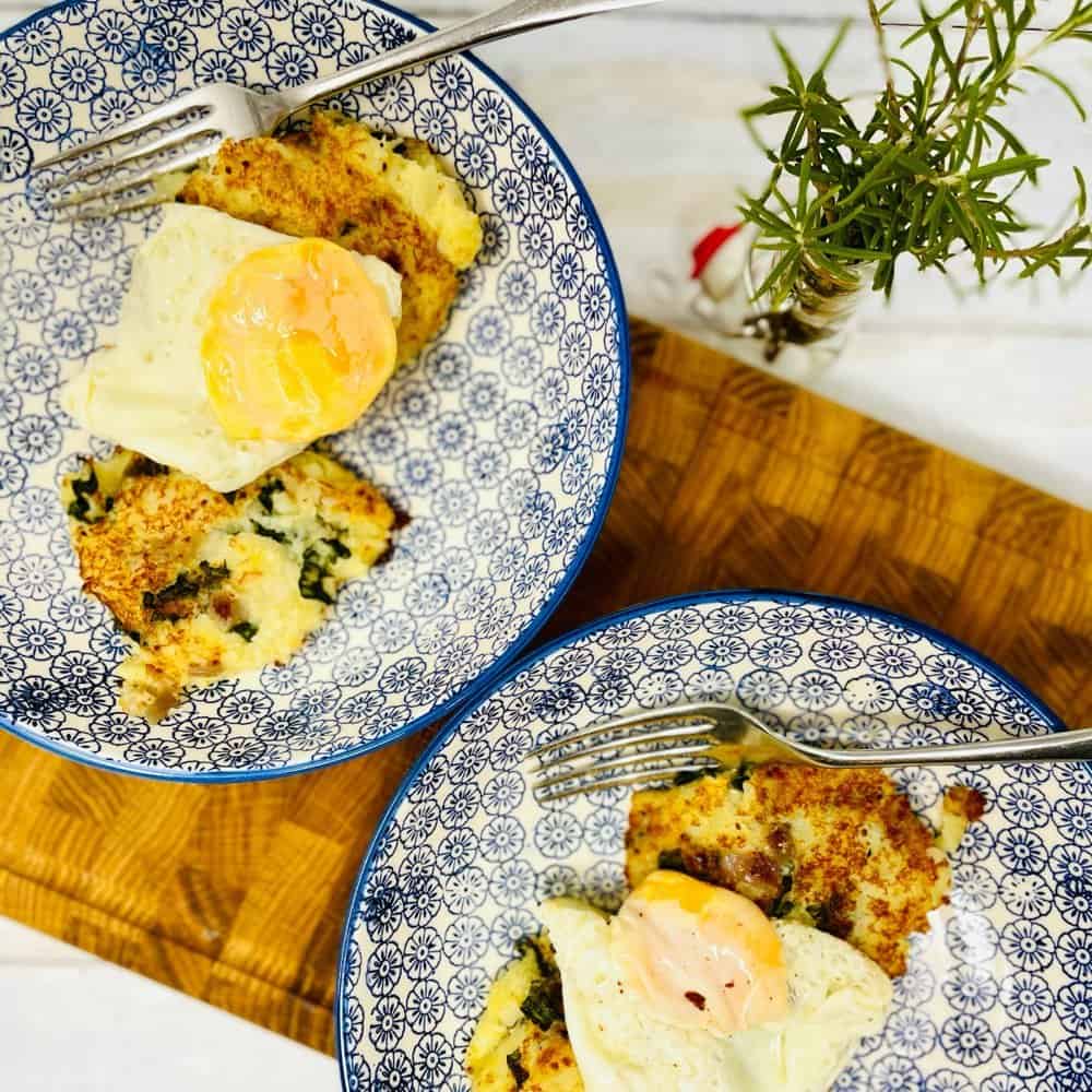An overhead view of two bubble and squeak topped with fried eggs placed in a blue and white bowl with rosemary on the side.