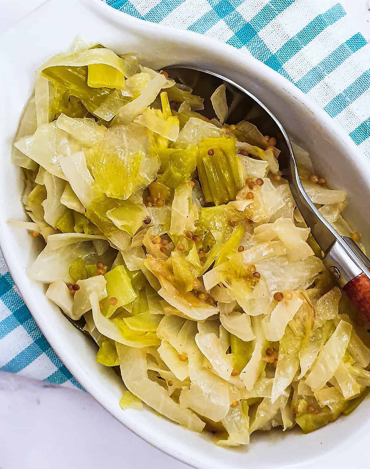Overhead view of a dish full of buttered cabbage with mustard seeds and leeks on top and a serving spoon.