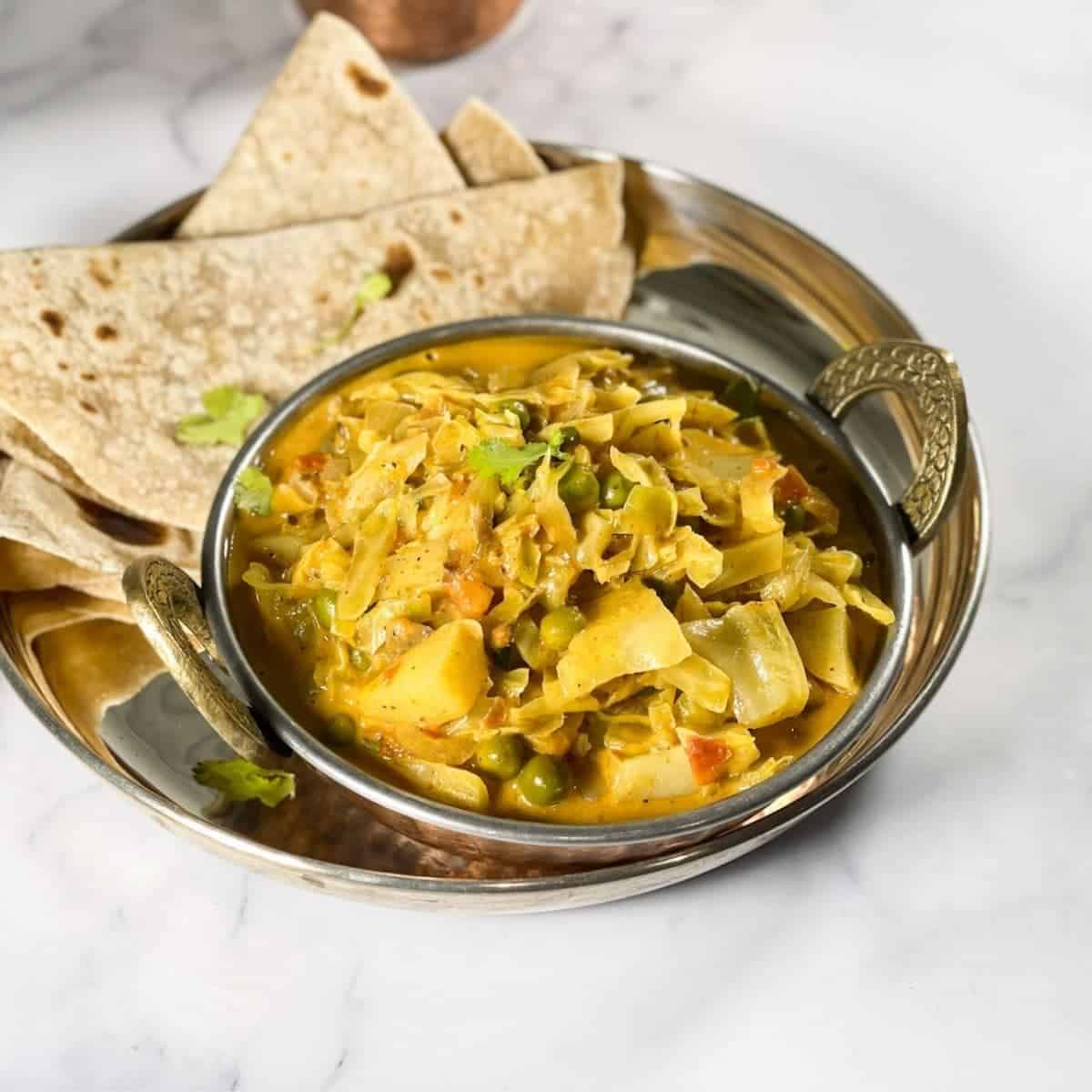 An overhead view of Indian cabbage curry placed in a copper bowl with chapati on the sides.