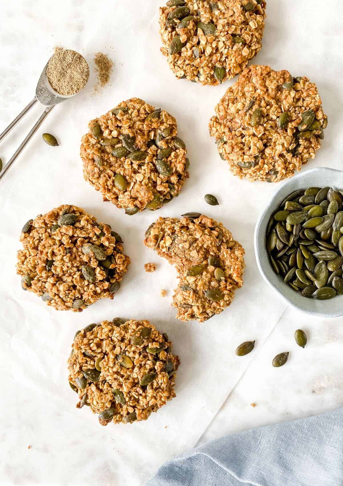 An overhead view of cardamom oatmeal cookies with a bowl of pumpkin seeds on the side. 