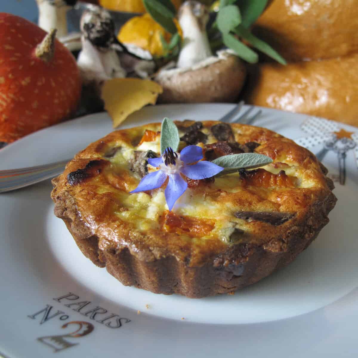 Straight shot of chestnut, pumpkin & mushroom tart with borage flower on top.