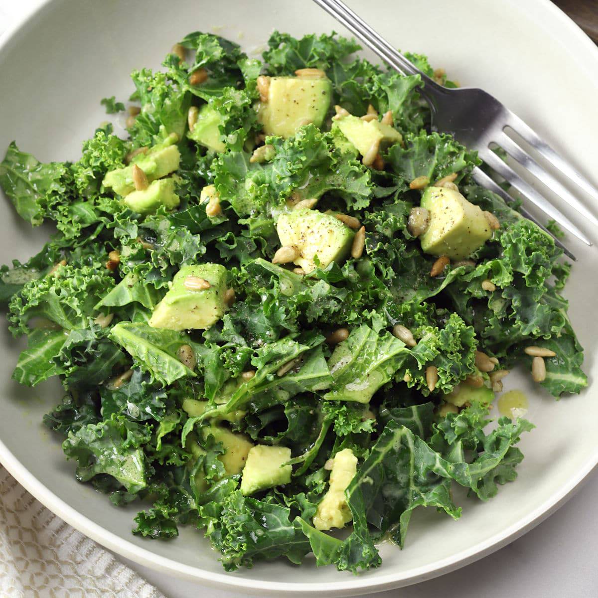 Overhead view of chopped kale avocado salad with homemade vinaigrette in a white bowl.