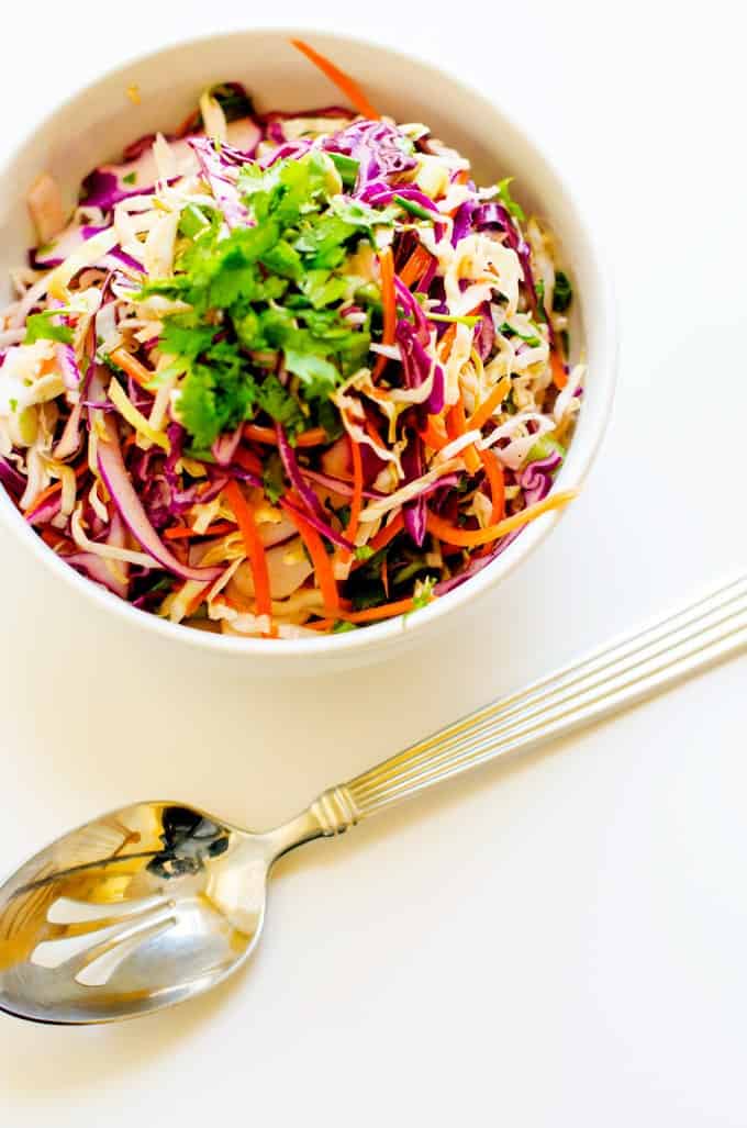 An overhead view of rainbow citrus slaw with parsley on top, placed in a white bowl next to a golden spoon.