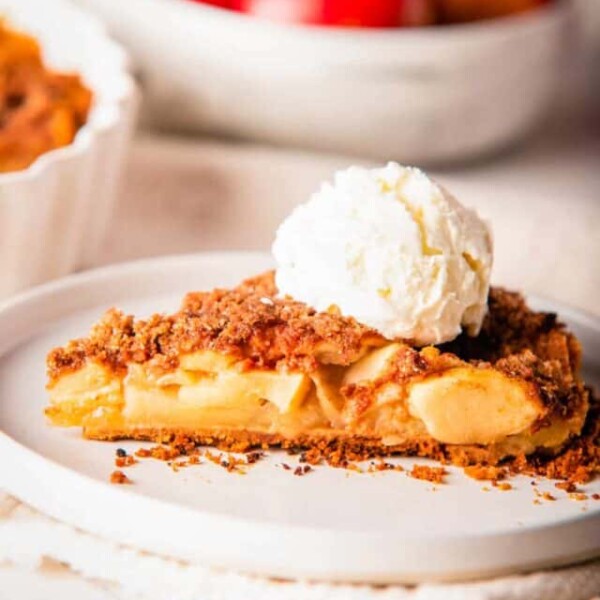 Close up view of apple pie slice with a dollop of ice cream on top, placed on a white plate.