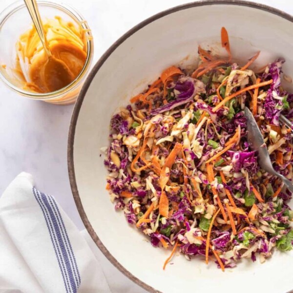 Mixed slaw in a large bowl with an empty bowl of peanut dressing on the side