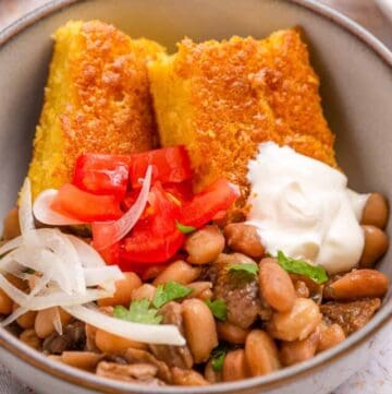 Close up of beans and cornbread in a white bowl with sour cream and onions on top.