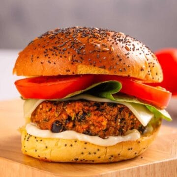 A close up image of black bean quinoa burger with tomatoes and lettuce on a cutting board.