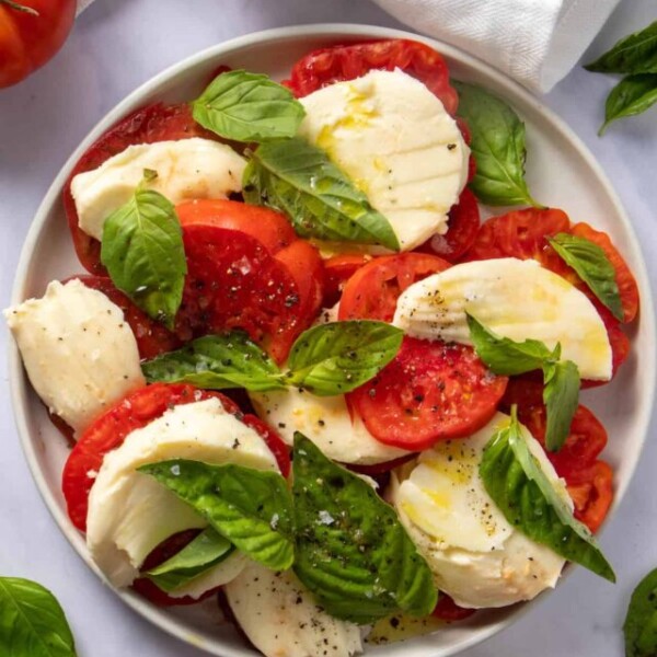 Plate with caprese salad (tomato, mozzarella and basil with olive oil, salt and pepper) as well as some garnishes on the side