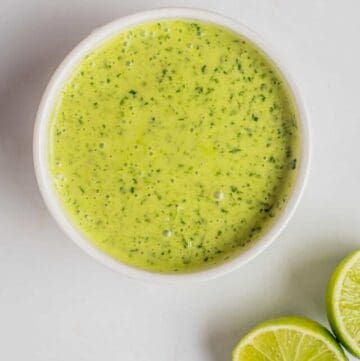 An overhead image of cilantro lime dressing in a small bowl with sliced limes on the side.