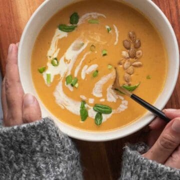 Person in fuzzy sweater holding a bowl of soup with a spoon