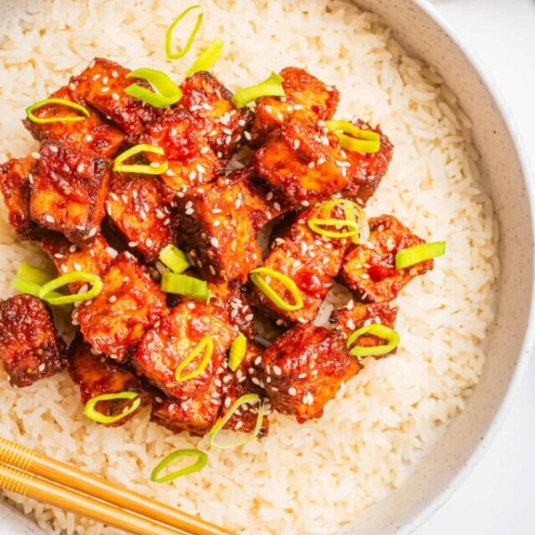 A close up image of gochujang tofu served on top of a bowl of rice with chopsticks on the side.