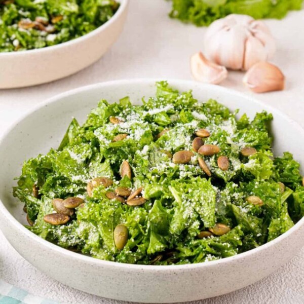 Side angle view of finished salad with white bowl with extra bowls of salad in the background.