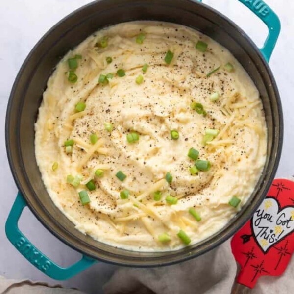 Dutch Oven with cheesy mashed potatoes in them with a spatula on side