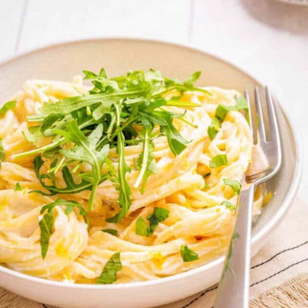Close-up view of one pot lemon ricotta pasta topped with chopped basil and rocket leaves placed on a plate with a fork on the side.