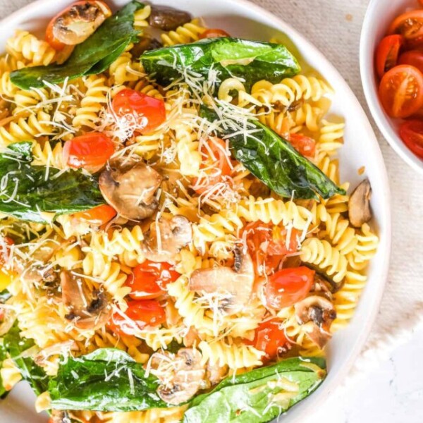 An overhead view of pasta fresca on a white plate with mushrooms and tomatoes next to it.