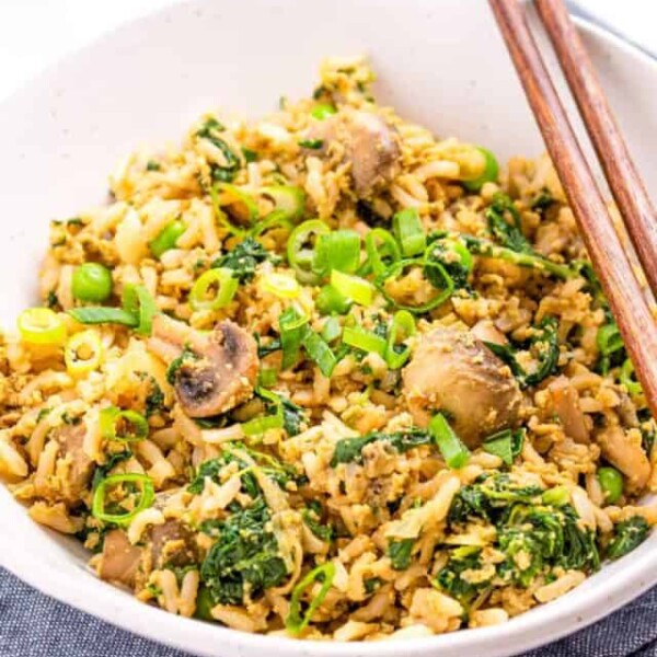 Side angle close up of fried rice in a white bowl with brown chopsticks on the rim.