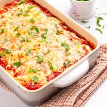An image of spaghetti squash lasagna in a white baking dish with parsley on the side.
