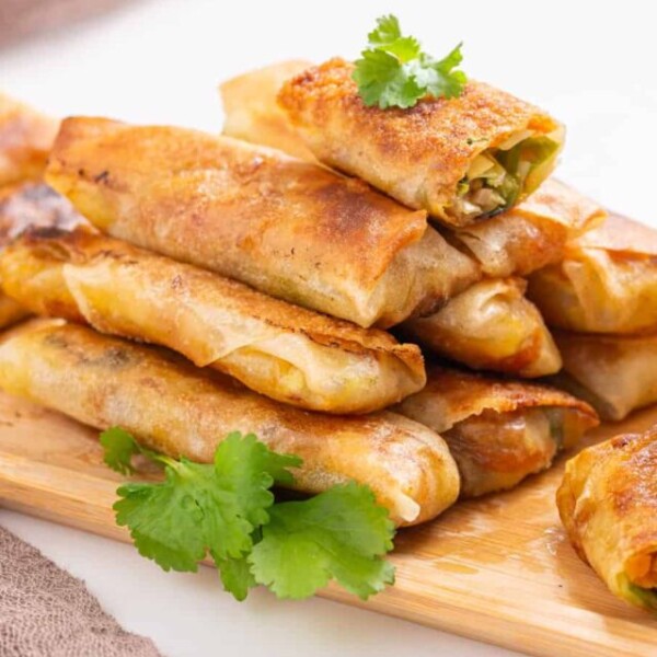 An image of vegan egg rolls arranged on a serving dish with sweet chili sauce on the side.